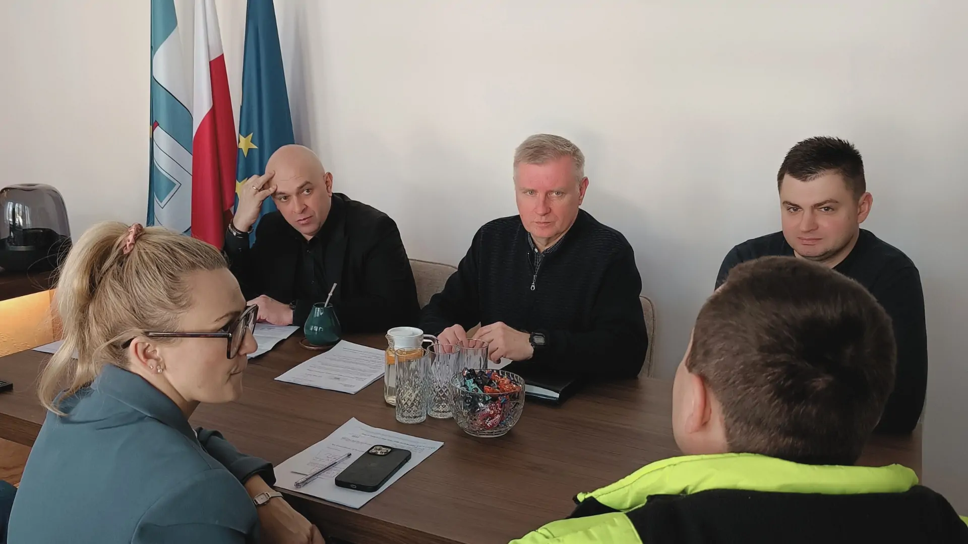 5 osób siedzących przy stole. Rozmawiają. Na stole leżą dokumenty.