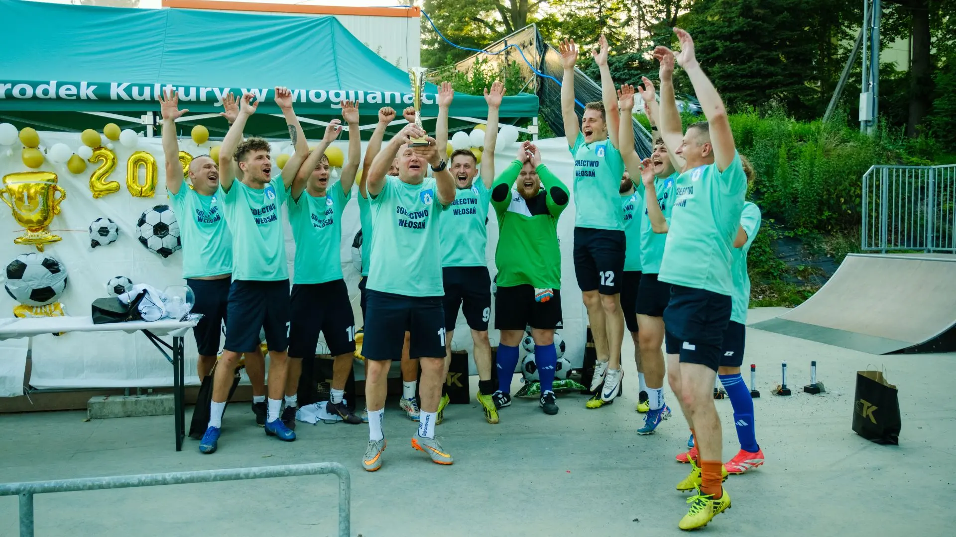 Zdjęcie zwycięzców turnieju po otrzymaniu pucharu. Mężczyźni radośnie podskakują i trzymają uniesiony puchar.
