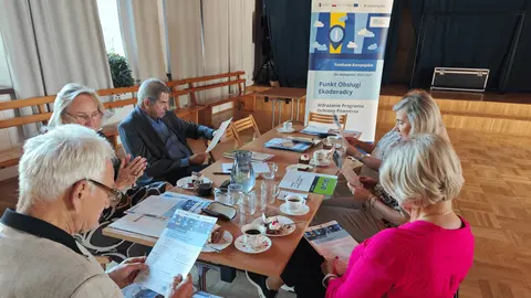 spotkanie Seniorów przy stole, w rękach trzymają ulotki
