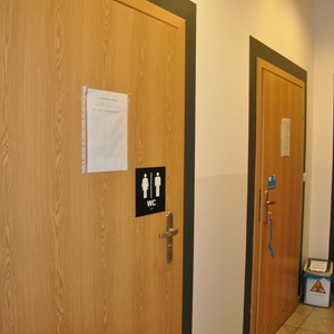 Drzwi ogólnodostępnej toalety oznaczone tabliczką z kontrastowym piktogramem, napisem WC i odwzorowaniem tyflograficznym.