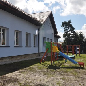 Nowy plac zabaw na tle błękitnej elewacji przedszkola.